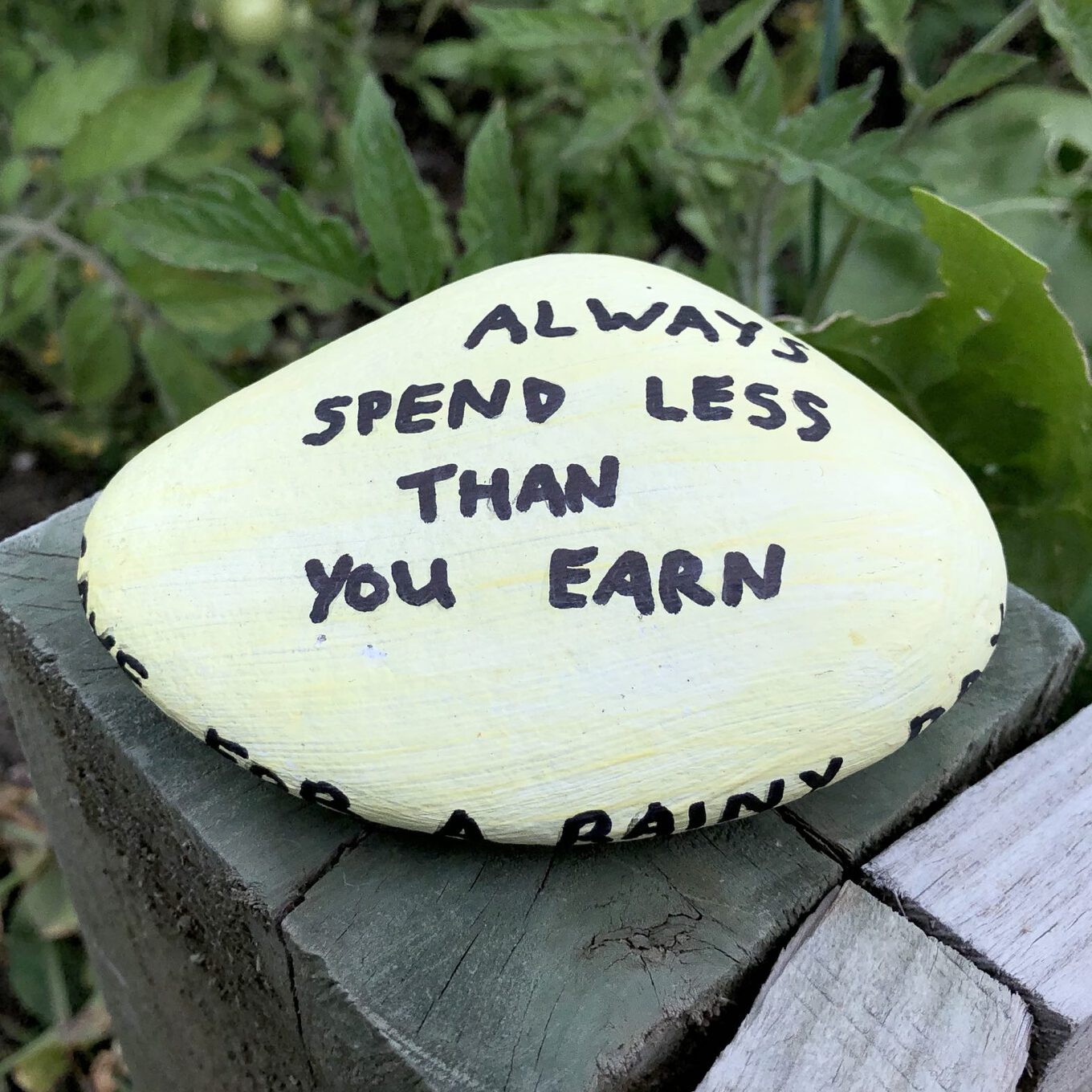 Ruth and her daughter have painted rocks with positive money messages to put in their garden A painted rock that says "Always spend less than you earn"